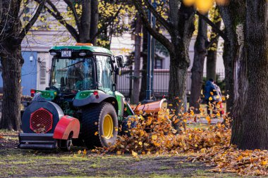 Riga, Letonya - 6 Kasım 2020: Hava üfleyicili bir traktör şehir parkının çimlerini temizliyor ve sonbahar yapraklarını uçuruyor