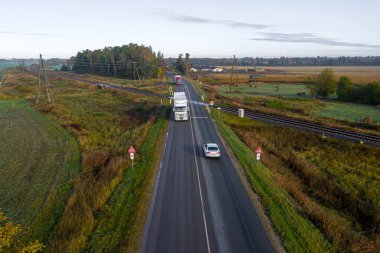 Jaunberze, Letonya - 13 Ekim 2020: kamyonlarla asfalt bir yoldan geçen demiryolu raylarının hava görüntüsü