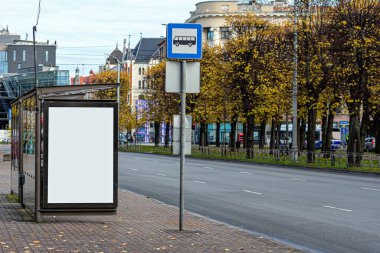 Kentteki otobüs durağında boş beyaz afiş, sonbahar günü kentsel ortamda kamuya açık bilgi panosu
