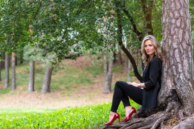 Zarif sarışın bayan ağaçların orada oturuyor ve sessizliğin tadını çıkarıyor.