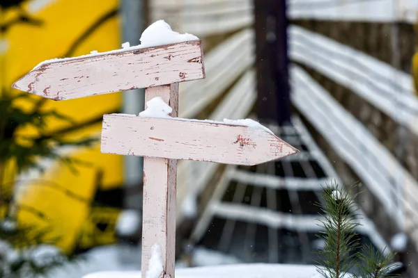 Renkli, bulanık bir arkaplanda iki kanatlı okları olan karlı tahta tabela direği.