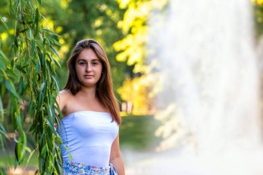 Güneşli bir günde, arka planda fıskiyesi olan genç bir kadının portresi.