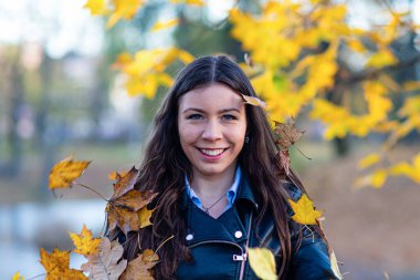 Çekici genç esmer, gülümseyen ve gökyüzüne akçaağaç yaprakları atan.