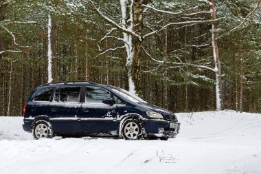 Riga, Letonya - 30 Ocak 2021: Mavi araba OPEL Zafira kış ormanına park etti