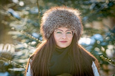 Soğuk bir kış ormanında gözlüklü ve beyaz elbiseli bir kadının portresi.