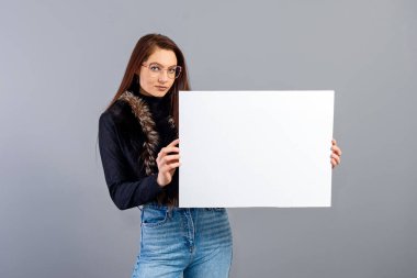 Zarif genç bir bayan, gri üzerinde izole edilmiş, fotokopi alanı ile boş tabela gösteriyor.
