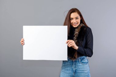 Duygusal genç bir kadın. Gri üzerinde izole edilmiş ve fotokopi alanı olan boş bir tabela gösteriyor.