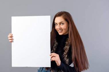 Duygusal genç bir kadın. Gri üzerinde izole edilmiş ve fotokopi alanı olan boş bir tabela gösteriyor.