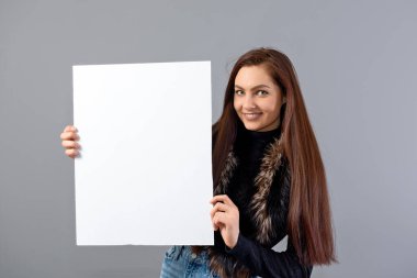 Duygusal genç bir kadın. Gri üzerinde izole edilmiş ve fotokopi alanı olan boş bir tabela gösteriyor.