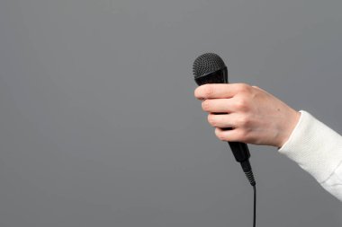 Gri arka planda mikrofonu olan kadın eli, yakın plan.