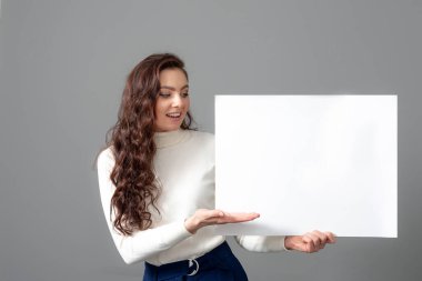 Uzun kıvırcık saçlı, güzel, şehvetli bir iş kadını boş bir reklam panosu gösteriyor.