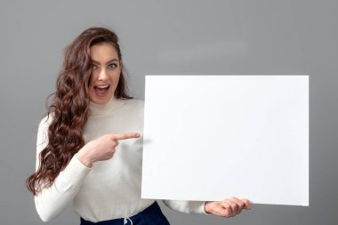 Uzun kıvırcık saçlı, güzel, şehvetli bir iş kadını boş bir reklam panosu gösteriyor.