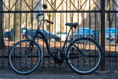 Güneşli bir günde metal bir çite yapıştırılmış klasik şehir bisikleti.