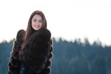 Sıcak kürklü neşeli genç kadın karlı ormanda kış gününün tadını çıkarıyor.