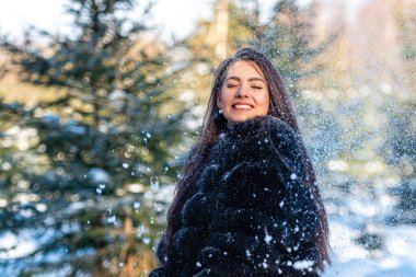 Sıcak kürklü neşeli genç kadın karlı ormanda kış gününün tadını çıkarıyor.