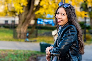 Güneşli bir günde, şehir parkındaki zayıf, duygusal, koyu renk saçlı genç bir kızın portresi. 