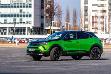 Riga, Letonya - 26 Mart 2021: yeşil elektrikli araç Opel Mokka-e kentsel yerleşim alanının arka planındaki otoparkta