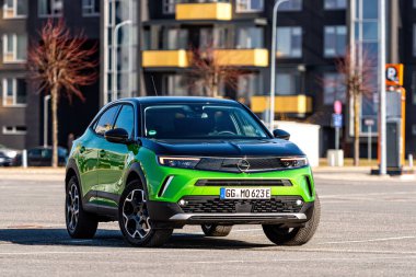 Riga, Letonya - 26 Mart 2021: yeşil elektrikli araç Opel Mokka-e kentsel yerleşim alanının arka planındaki otoparkta