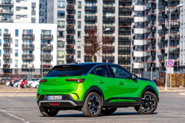Riga, Letonya - 26 Mart 2021: yeşil elektrikli araç Opel Mokka-e kentsel yerleşim alanının arka planındaki otoparkta