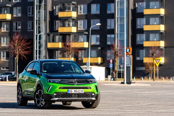 Riga, Letonya - 26 Mart 2021: yeşil elektrikli araç Opel Mokka-e kentsel yerleşim alanının arka planındaki otoparkta