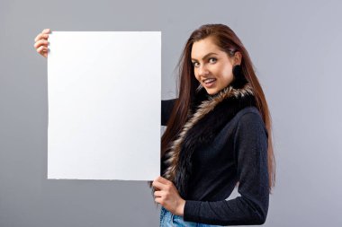 Zarif genç bir bayan, gri üzerinde izole edilmiş, fotokopi alanı ile boş tabela gösteriyor.
