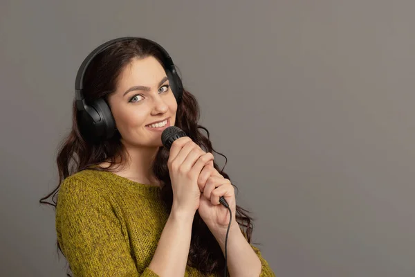 expressive teenager female singing with a microphone and headphones, isolated on gray