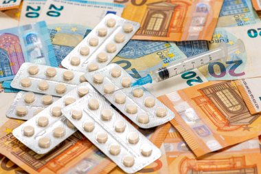 Avro banknotlarının arka planında tabletleri olan şırınga ve tablet, pahalı sağlık hizmeti maliyeti kavramı