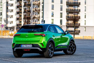 Riga, Letonya - 26 Mart 2021: yeşil elektrikli araç Opel Mokka-e kentsel yerleşim alanının arka planındaki otoparkta
