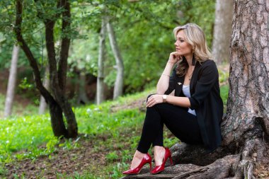 Zarif sarışın bayan ağaçların orada oturuyor ve sessizliğin tadını çıkarıyor.