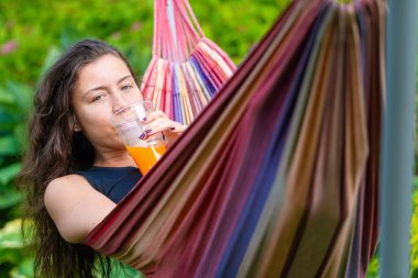 Harika kız hamakta uzanmış portakal suyu içiyor, bahçede dinleniyor.