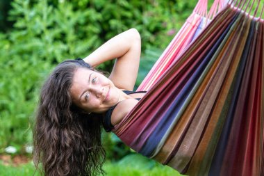Uzun siyah saçlı muhteşem genç kız bahçedeki bir hamakta sallanıyor ve flört ediyor.