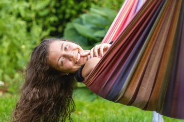 Uzun siyah saçlı muhteşem genç kız bahçedeki bir hamakta sallanıyor ve flört ediyor.