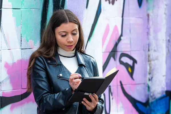 Young Woman Leans Wall Sprayed Graffiti Makes Notes Black Notebook — Stock Photo, Image