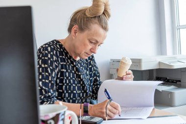 İşyerinde çalışan orta yaşlı bir ofis kadını işini bölmeden dondurma yiyor.