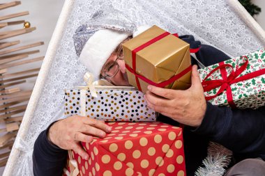 Orta yaşlı gözlüklü ve Noel hediyeli gümüş cüce şapkalı bir adam süslü bir odada, Noel konsepti