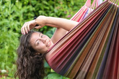 Uzun siyah saçlı muhteşem genç kız bahçedeki bir hamakta sallanıyor ve flört ediyor.
