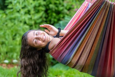 Uzun siyah saçlı muhteşem genç kız bahçedeki bir hamakta sallanıyor ve flört ediyor.