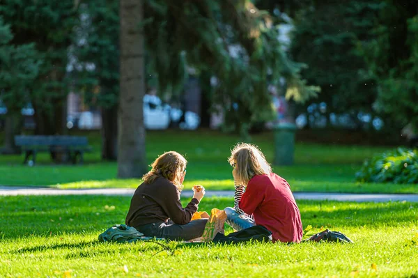 Riga, Letonya - 3 Eylül 2021: Son ılık sonbahar günlerinde genç kızlar şehir merkezindeki parkta çimlerin üzerinde yemek yiyorlar.
