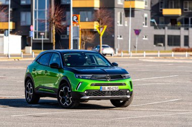 Riga, Letonya - 26 Mart 2021: yeşil elektrikli araç Opel Mokka-e kentsel yerleşim alanının arka planındaki otoparkta