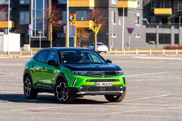 Riga, Letonya - 26 Mart 2021: yeşil elektrikli araç Opel Mokka-e kentsel yerleşim alanının arka planındaki otoparkta