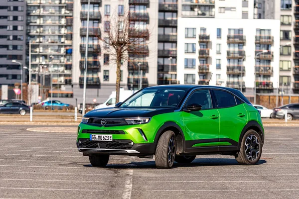 Riga, Letonya - 26 Mart 2021: yeşil elektrikli araç Opel Mokka-e kentsel yerleşim alanının arka planındaki otoparkta
