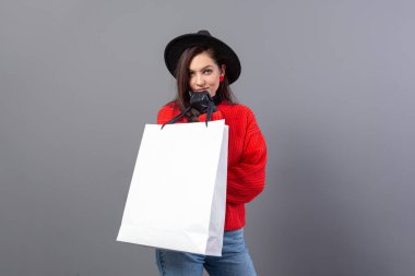 Kırmızı kazaklı, siyah şapkalı, alışveriş çantalı çekici bir kadın. Gri renkte izole edilmiş, fotokopi odası.