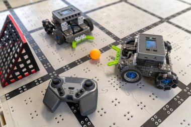 İki robot masadaki bir ızgarada geziniyor ve yakınlardaki bir kontrolörle eğlenceli bir aktiviteye girişiyor..