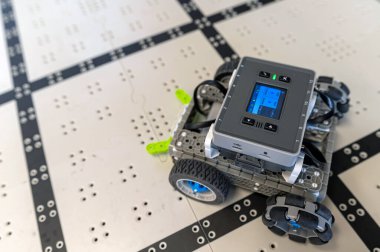 Küçük bir robot şebeke benzeri bir yolda yol alıyor, teknolojisini ve sensörlerini gösteriyor..