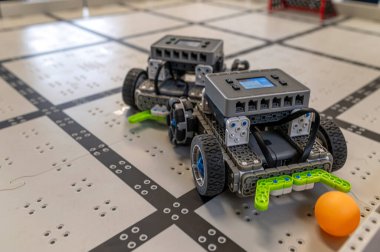 İki küçük robot, şebeke desenli bir katta, bir top içeren bir göreve hazırlar..