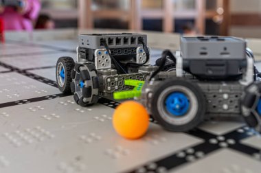 Robotlar şebeke yüzeyinde hareket eder, bir teknoloji sergisi sırasında topla karşılaşırlar..