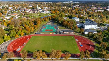 Dobele, Letonya - 9 Ekim 2025: Dobele, Letonya 'da renkli ağaçlarla çevrili spor alanlarını gösteren hava görüntüsü.