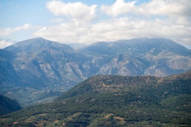 Yuvarlanan tepeler ve görkemli dağlar Girit 'te ziyaretçileri dinamik bulutlar altında karşılıyor..