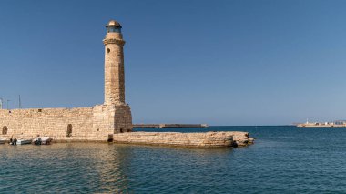 Deniz feneri gururla kıyıda durur, berrak mavi gökyüzü ve durgun sularıyla Rethymno 'da.