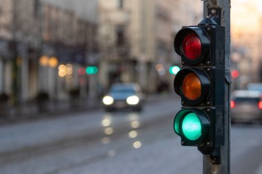 Semforlu ışıklar yeşil, sarı ve kırmızı renkleri gösteriyor. Arabalar işlek cadde bölgesinden geçiyor..